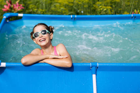 Cute teenage girl relaxing in the pool in her backyard, laughing and swimmingの写真素材