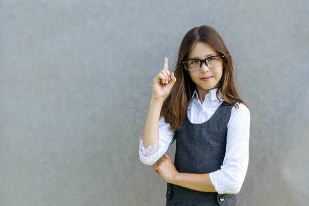 Close-up portrait of a teenage girl in glasses in a school uniform on a gray background, the concept of school and studyの写真素材