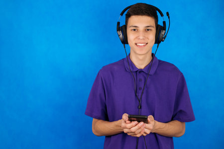 Young guy in headphones and with a phone on a blue background, listens to music, communicates online...
