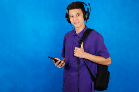 Portrait of a young student with a school bag, smartphone and headphones. The teenager smiles and looks at the camera.の写真素材