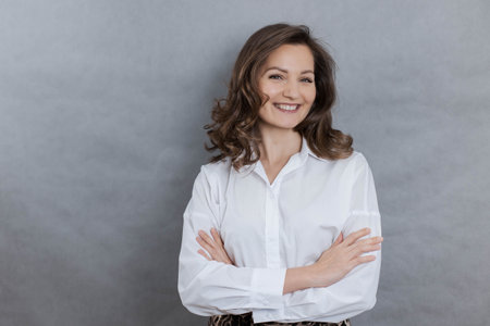 Beautiful young businesswoman smiles and crosses her arms over her chest, looking at the camera, copy spaceの写真素材