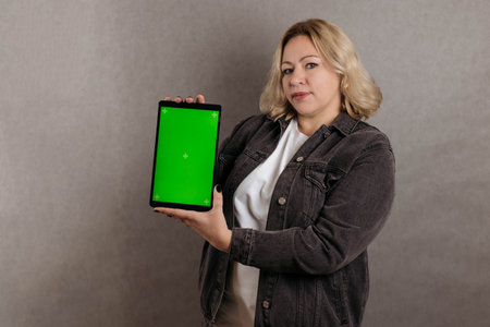 Portrait blonde plus close-up size on a gray background, holding a smartphone with a green screen. Copy space, chroma keyの写真素材