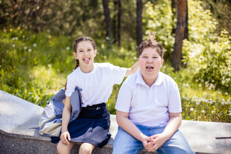 Close-up portrait of two teenagers sitting on a bench, laughing, looking at the camera and showing their tongue.の写真素材