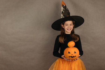 Close-up portrait of a pretty girl in a Halloween costume, holding two pumpkins, on a gray...