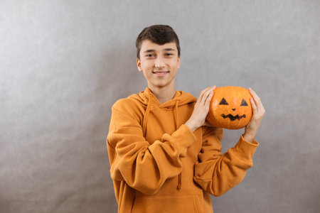 Protret a sypatic young man with a pumpkin to Halloween in his hands on a gray background. Copy spaceの写真素材