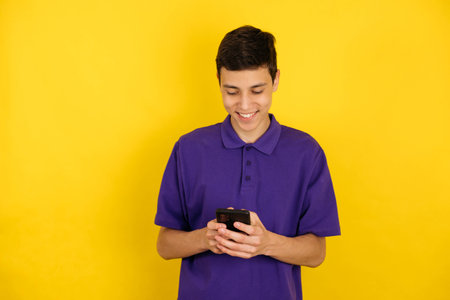 Close-up portrait of a young man with a smartphone in his hands on a yellow background, copy space, looks downの写真素材