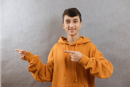 Attractive young man pointing hands to left on gray background, copy spaceの写真素材