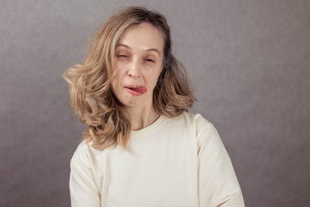Funny portrait of a young woman, laughing and sticking out her tongue. Gray background, copy space