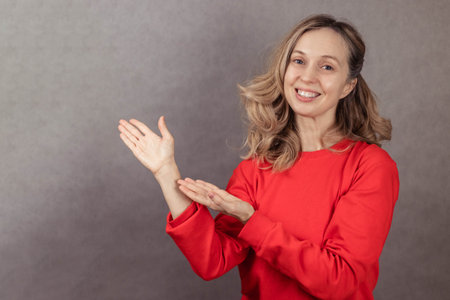 Close-up portrait of young woman on gray background, pointing hands to the side and looking at...