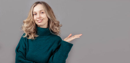 Young woman pointing her hand to the side, looking at camera, smiling, banner on gray background
