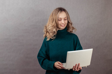 Close-up portrait of a young woman on a gray background, holding a laptop in her hands, looking at the screenの写真素材