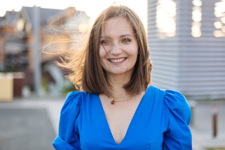 Close-up portrait of a young woman at sunset in the city, with her hair blowing in the windの写真素材
