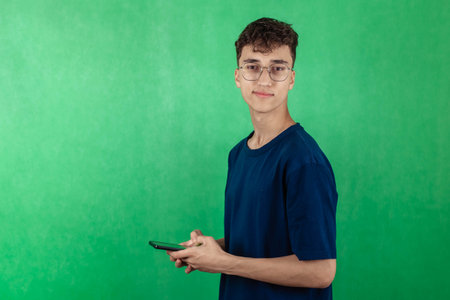 Young guy student wearing glasses on green background, holding phone, chroma ke, copy space