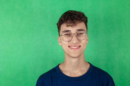 Close-up portrait of young man in glasses, smiling and looking at camera, green backgroundの写真素材