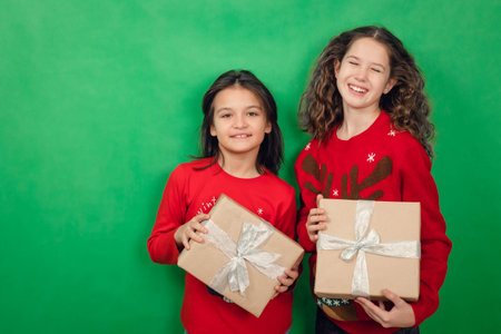Two charming girls in red jumpers and with gifts in their hands, smiling and looking at camera on green background,の写真素材