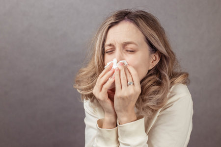 Female individual is holding tissues to her face, showing signs of discomfort in a softly lit indoor...