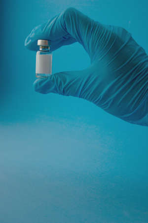 A hand in a blue medical glove holds an ampoule on a blue background.の写真素材