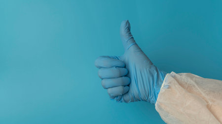 Hand in blue silicone glove and a protective suit on blue background shows the sign OK. Protection concept. COVID-19.の写真素材