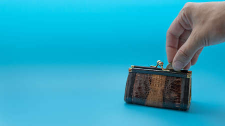 A woman's hand lowers a coin into a small vintage purse, on a blue backgroundの写真素材
