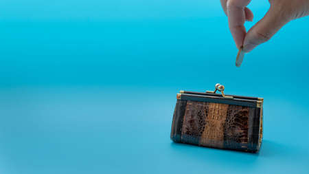 A woman's hand lowers a coin into a small vintage purse, on a blue backgroundの写真素材