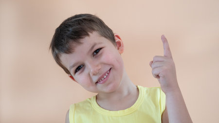 Cute stylish boy in a yellow T-shirt on a peach background, shows a finger gestureの写真素材