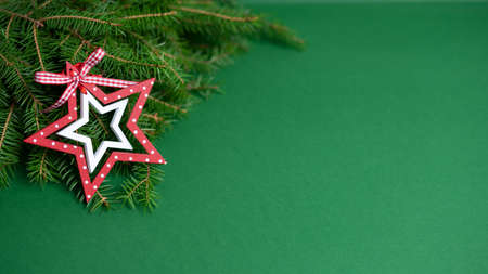 A natural bouquet of fir branches and a toy wooden red-white star, lie on a green backgroundの写真素材