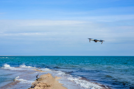 Drone flying in the sky above the waves of the blue sea, which splash on the sandy shore.