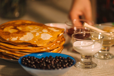 A stack of thin Russian hot pancakes blini  with currants, honey, sour cream and jam.