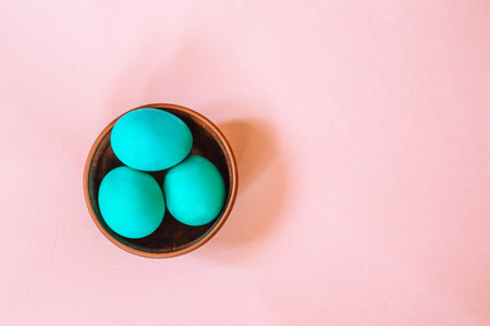 Three Easter eggs of turquoise color in a wooden plate on a soft pink background.の写真素材