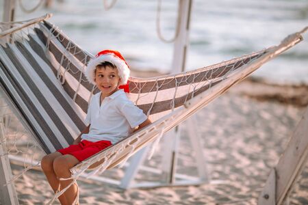 Boy in a santa hat on the beach with a Christmas tree.の写真素材