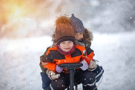 Happy two brothers family have fun sledding in a snowy forest in the mountains in winter.