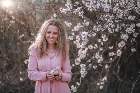 Spring photo of a beautiful young girl near flowering trees holding eggs in her hands. .
