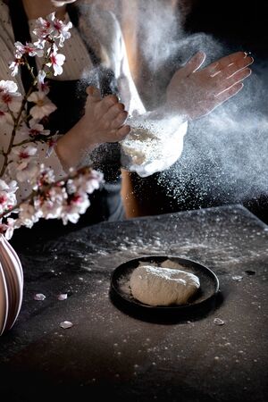 Womans hands knead the dough on the table with flour and ingredients.の写真素材