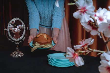 Hands of a girl with Easter cake on a blue dish are held out against a black background.の写真素材