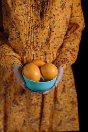 Woman's hands in an orange dress hold a blue plate with ripe lemons. Natural healthy food.