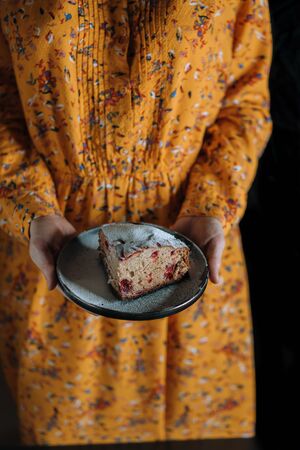In the hands of a girl in an orange dress on a black plate is a piece of cake. Culinary concept.の写真素材