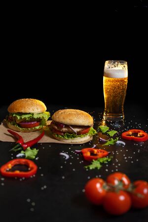 Two fresh hamburger with steak, salad on a background of blurred glass of light beer on a black background.の写真素材