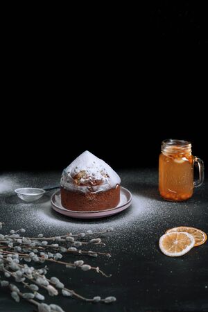 Easter cake with icing sugar on a dark background, sea buckthorn tea, slices of orange and sprigs of willow on the table next to it. Easter concept.の写真素材