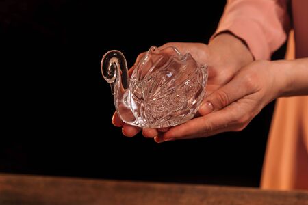 Crystal swan in female hands in a pink dress, over a wooden background, on a black background.の写真素材