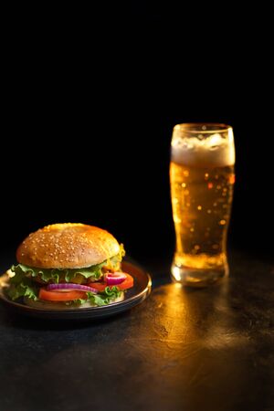 Fresh hamburger with steak, lettuce on the background of a blurred glass of light beer on a black background. Home delivery food.の写真素材