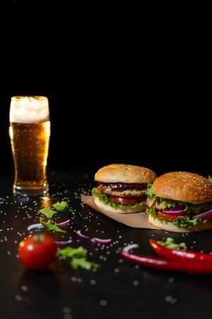 Two fresh hamburger with steak, salad on a background of blurred glass of light beer on a black background.の写真素材