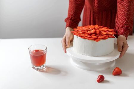 Homemade white birthday cake decorated with strawberries. Food concept. Cream cheese pink wedding cake on a white background. Woman holds a delicious cake.の写真素材
