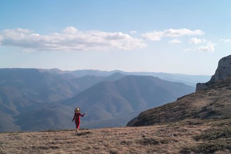 Young beautiful woman in a red dress looking at the mountains. Girl on nature on a background of blue sky. Fashion photoの写真素材