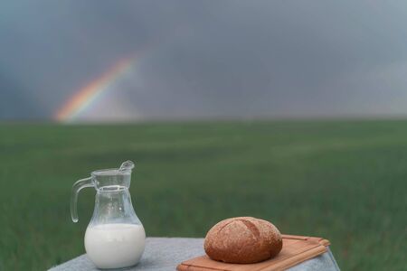 Still life with bread and milk on a table in the middle of a green field and blue sky.の写真素材