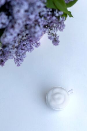A cup of morning drink with whipped cream on a background of a bouquet of lilacs in a pink vase.の写真素材