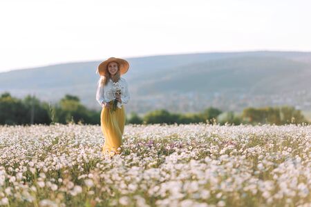 Beautiful girl in a yellow dress on a field of daisy flowers.の写真素材