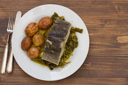 fish with potato and vegetables on white plate and glass of water on brown backgroundの写真素材