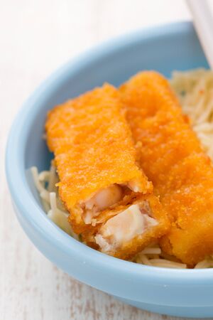fish sticks with pasta in blue bowl on white wooden backgroundの写真素材