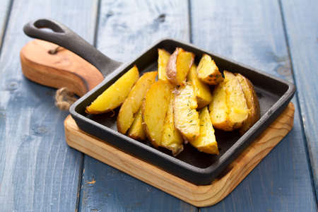 fried potato on black frying pan on blue wooden background