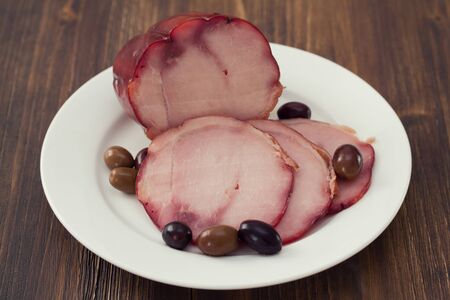 smoked meat with olives on white plate on wooden backgroundの写真素材